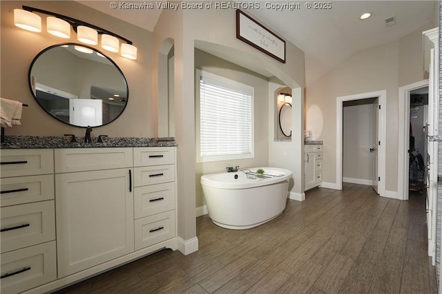 bathroom featuring vaulted ceiling, wood-type flooring, a washtub, and vanity