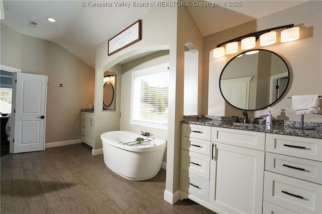 bathroom featuring vaulted ceiling, a tub, and vanity