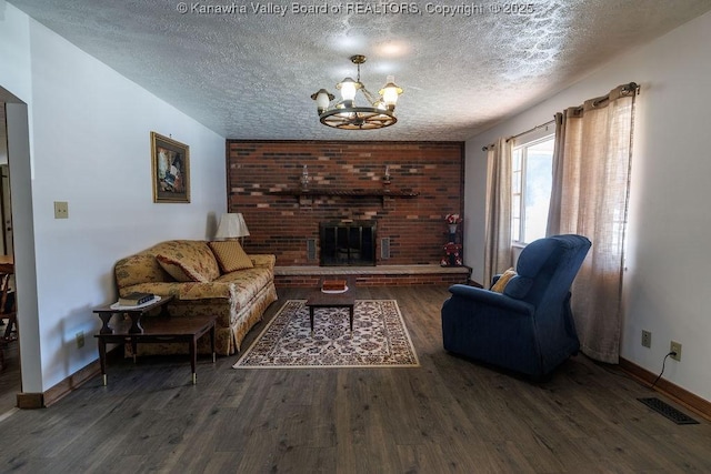 living room featuring an inviting chandelier, dark hardwood / wood-style flooring, a brick fireplace, and a textured ceiling