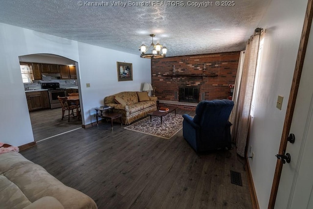 living room with a notable chandelier, dark hardwood / wood-style floors, a fireplace, and a textured ceiling