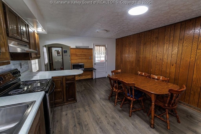 dining room with dark wood-type flooring, a textured ceiling, and wood walls