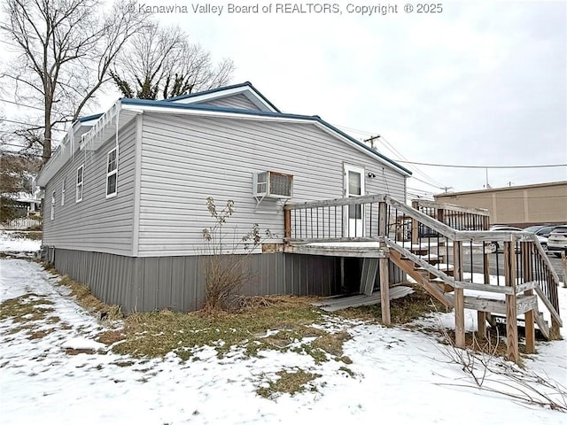 snow covered back of property featuring a deck and a wall unit AC