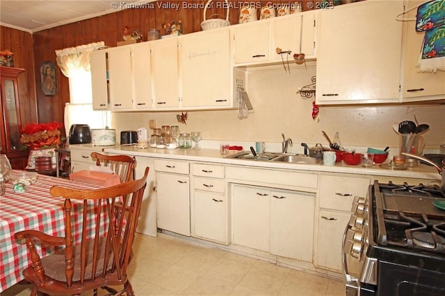 kitchen with gas stove, sink, wood walls, crown molding, and white cabinets