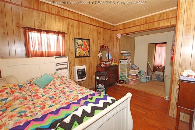 bedroom featuring heating unit, hardwood / wood-style flooring, and wooden walls