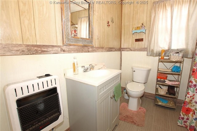 bathroom with vanity, toilet, heating unit, and wood walls