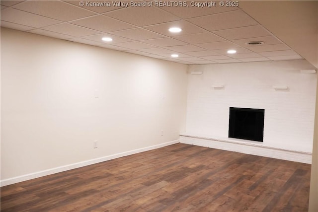 empty room with wood-type flooring, a brick fireplace, and a drop ceiling