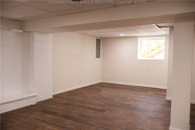 basement featuring a drop ceiling, dark wood-type flooring, and electric panel