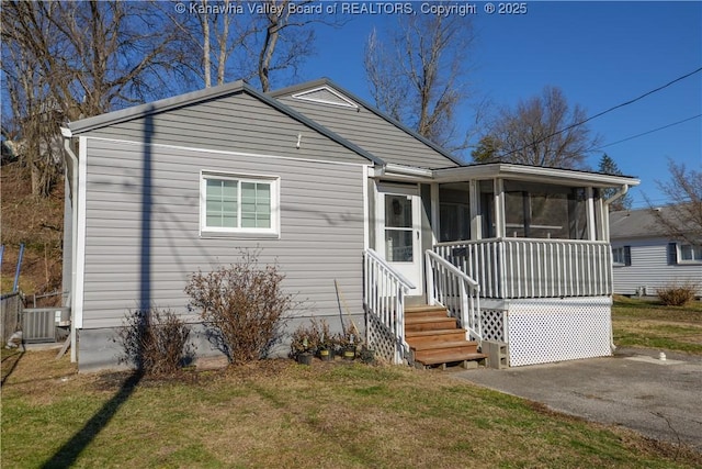 view of front facade featuring central AC, a front lawn, and a sunroom