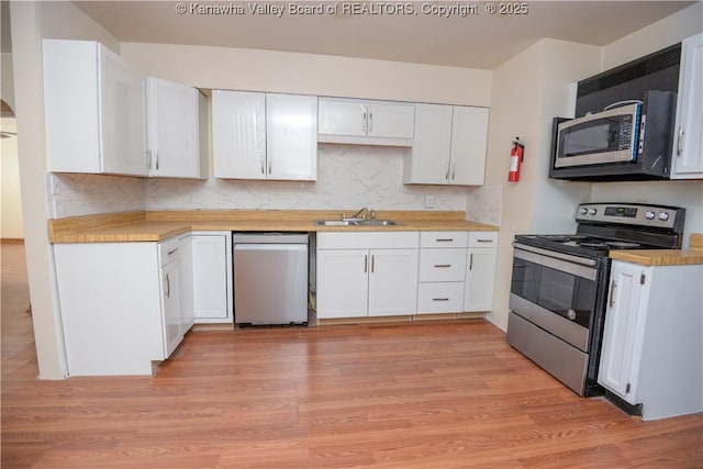 kitchen with white cabinetry, sink, backsplash, stainless steel appliances, and light hardwood / wood-style flooring