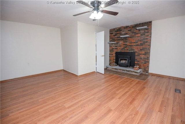 unfurnished living room featuring a wood stove, ceiling fan, and light wood-type flooring