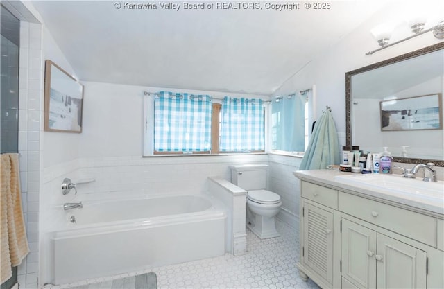 bathroom featuring toilet, vaulted ceiling, tile walls, vanity, and a bathing tub