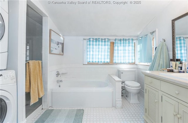 bathroom with toilet, vaulted ceiling, vanity, a tub, and stacked washer / dryer