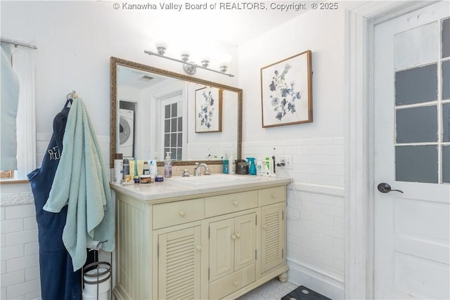 bathroom featuring vanity, stacked washing maching and dryer, tile patterned flooring, and tile walls