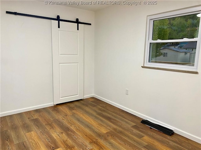 unfurnished bedroom featuring dark hardwood / wood-style flooring and a barn door