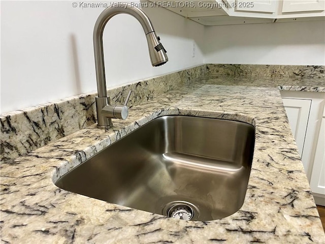 room details with sink, white cabinets, and light stone counters