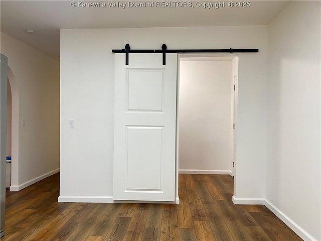 unfurnished bedroom featuring a closet, dark hardwood / wood-style floors, and a barn door