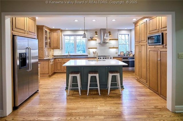 kitchen with wall chimney range hood, a breakfast bar, stainless steel appliances, a center island with sink, and decorative backsplash