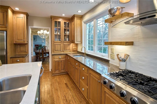 kitchen featuring sink, dark stone counters, light wood-type flooring, stainless steel appliances, and wall chimney range hood