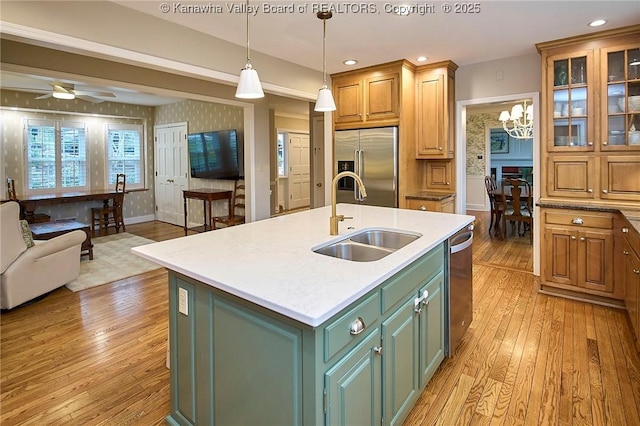 kitchen featuring sink, green cabinets, a kitchen island with sink, stainless steel appliances, and light wood-type flooring