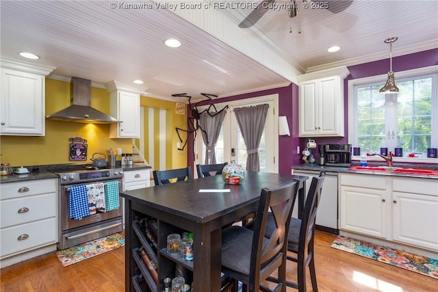 kitchen with appliances with stainless steel finishes, white cabinets, light hardwood / wood-style floors, and wall chimney exhaust hood