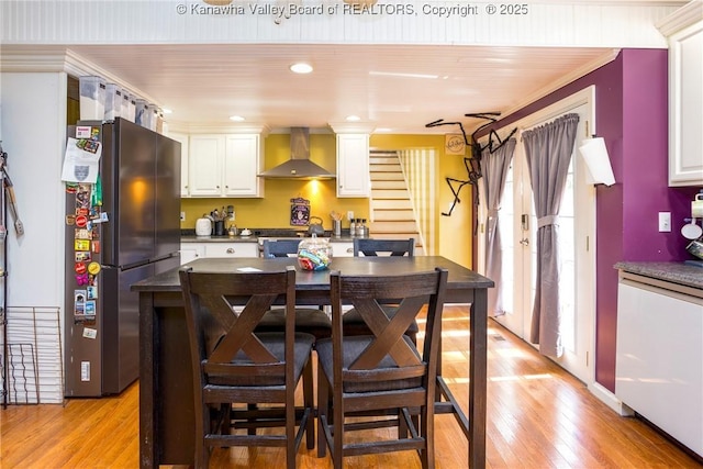 kitchen with wall chimney exhaust hood, black fridge, crown molding, light wood-type flooring, and white cabinets