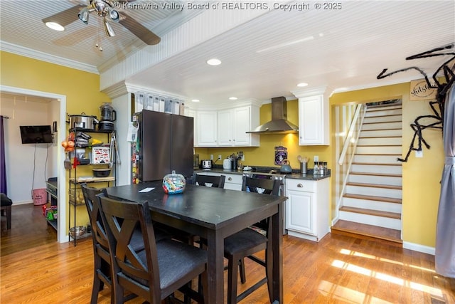 kitchen with wall chimney range hood, stainless steel fridge, ornamental molding, and white cabinets