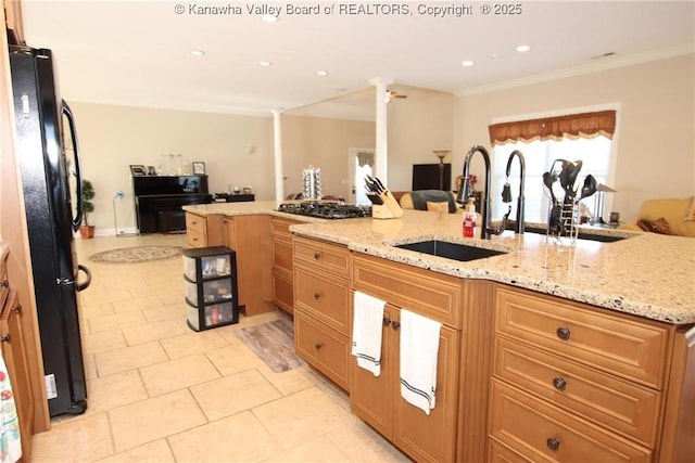 kitchen featuring a breakfast bar, decorative columns, sink, black fridge, and light stone countertops