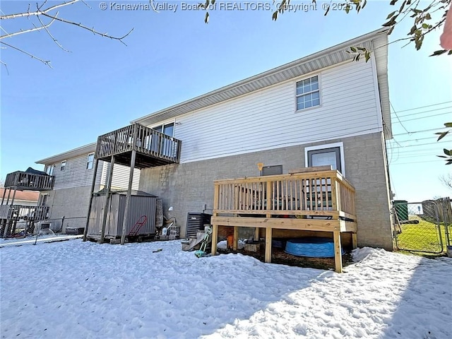 snow covered rear of property with a wooden deck and cooling unit