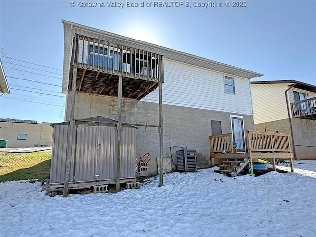 snow covered back of property with a wooden deck, a storage shed, and central AC unit