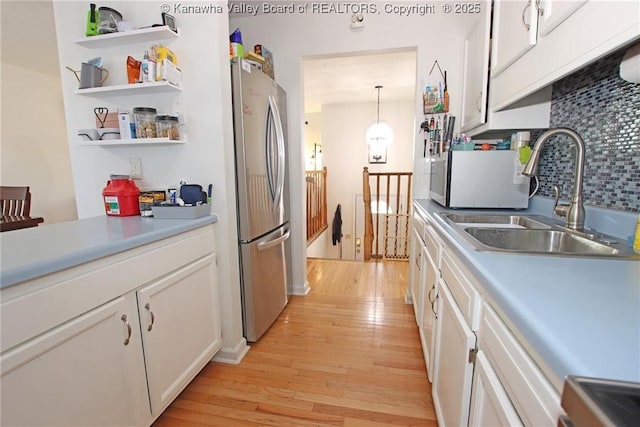 kitchen with pendant lighting, white cabinetry, sink, stainless steel fridge, and light hardwood / wood-style floors