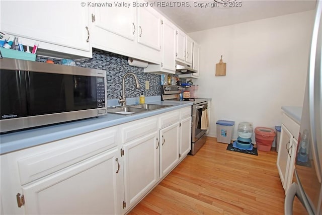 kitchen featuring appliances with stainless steel finishes, tasteful backsplash, white cabinetry, sink, and light wood-type flooring