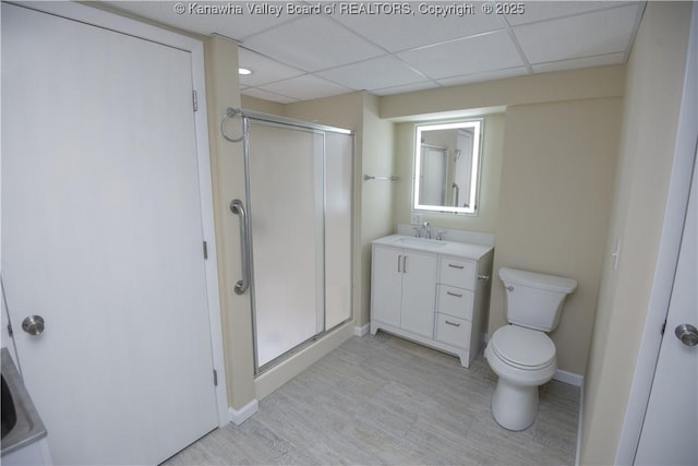 bathroom featuring vanity, a shower with shower door, toilet, and a drop ceiling