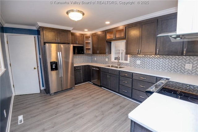 kitchen featuring wall chimney exhaust hood, dark brown cabinets, light hardwood / wood-style flooring, ornamental molding, and appliances with stainless steel finishes