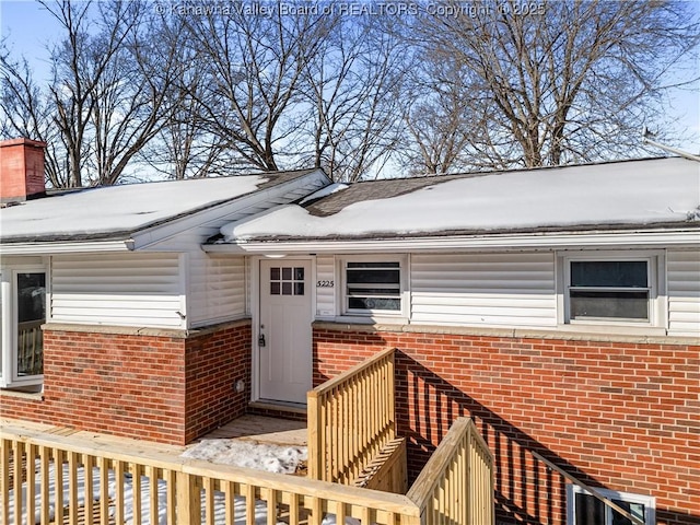 snow covered property entrance with a wooden deck