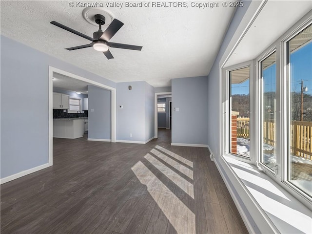 unfurnished living room featuring dark wood-type flooring, ceiling fan, sink, and a textured ceiling