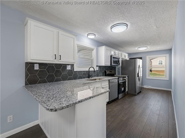 kitchen featuring sink, appliances with stainless steel finishes, white cabinetry, light stone counters, and tasteful backsplash