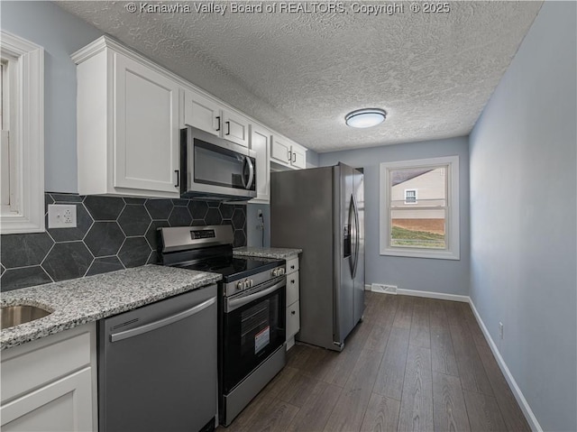 kitchen featuring stainless steel appliances, white cabinetry, tasteful backsplash, and light stone counters