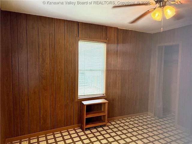 empty room featuring ceiling fan and wood walls