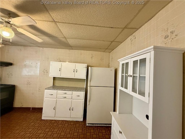 kitchen featuring white fridge, a drop ceiling, white cabinets, and ceiling fan