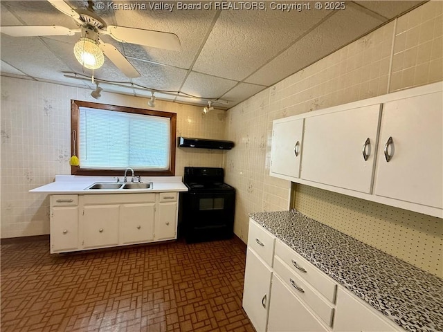 kitchen with black electric range oven, sink, a paneled ceiling, white cabinetry, and tile walls