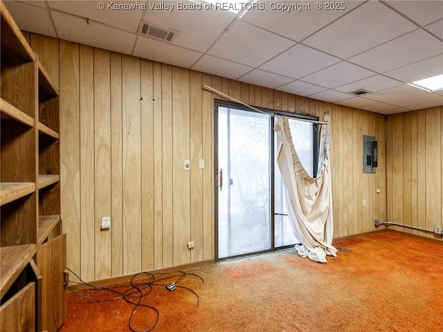 unfurnished room with carpet floors, a drop ceiling, electric panel, and wooden walls