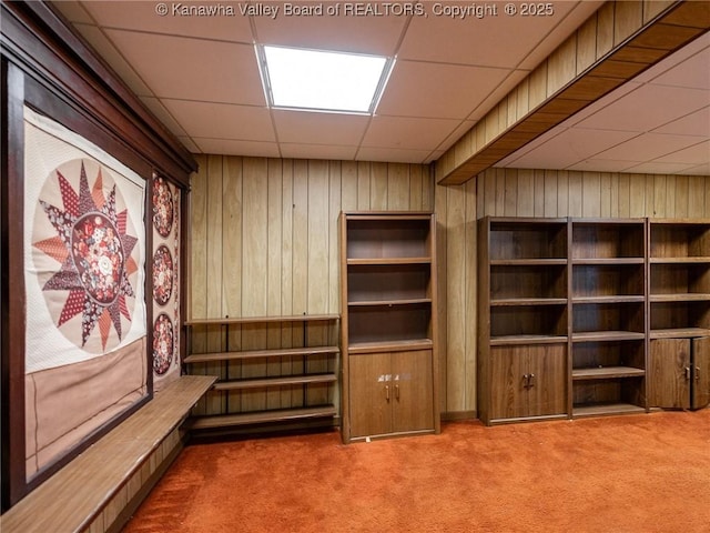 interior space featuring a paneled ceiling, carpet flooring, and wood walls