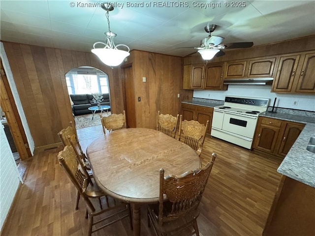 dining room featuring dark hardwood / wood-style floors, ceiling fan, and wood walls