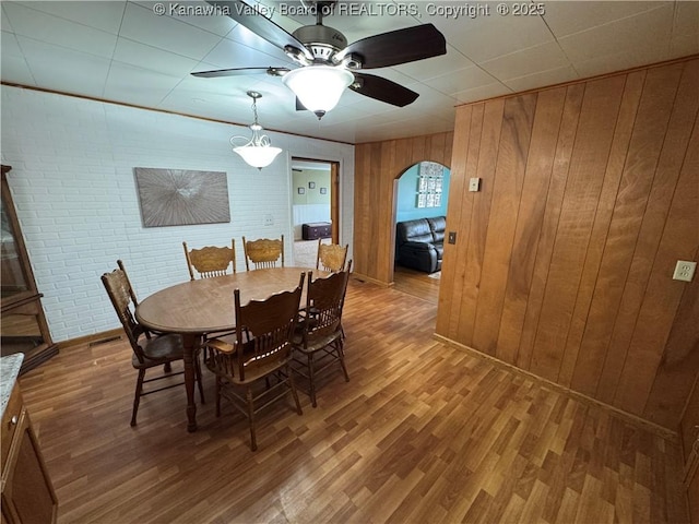 dining space with hardwood / wood-style floors, wooden walls, ceiling fan, and brick wall