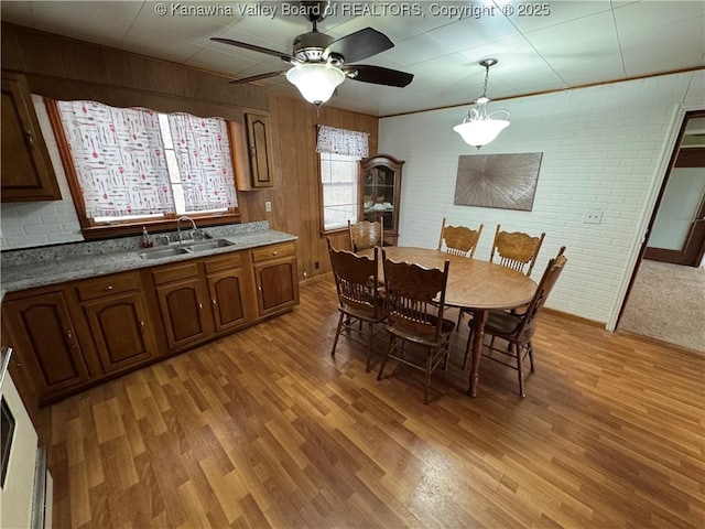 dining area featuring sink, light hardwood / wood-style flooring, ceiling fan, and brick wall