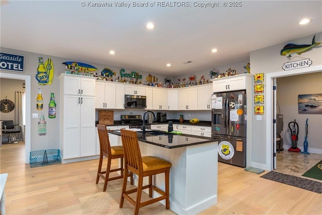 kitchen featuring white cabinetry, appliances with stainless steel finishes, light hardwood / wood-style floors, and a center island with sink