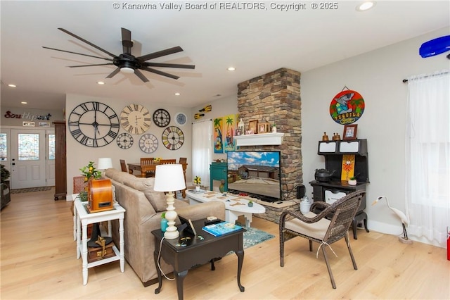 living room featuring ceiling fan, a stone fireplace, and light hardwood / wood-style floors