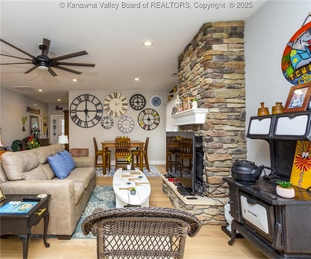 living room featuring a stone fireplace, ceiling fan, and light wood-type flooring