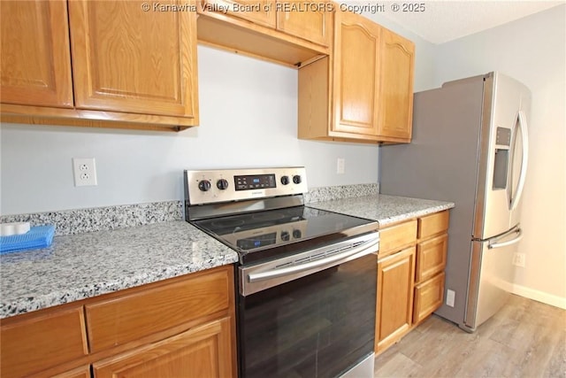 kitchen with appliances with stainless steel finishes, light stone countertops, and light hardwood / wood-style flooring