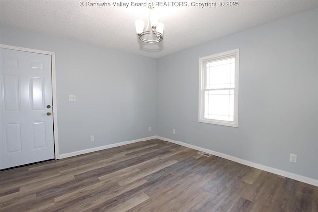 empty room featuring dark hardwood / wood-style floors, a notable chandelier, and a textured ceiling